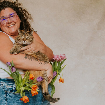 Plus size women with glasses wearing jeans and a white shirt holding tulips