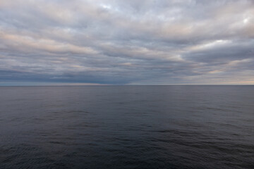 View from cruise ship balcony looking out at a calm still endless ocean horizon. Beautiful dark pastel cloudscape 