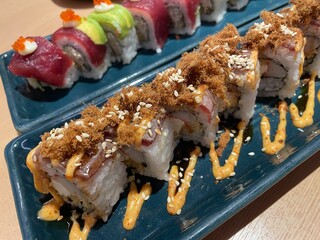 A close-up, top-down view showcases two rows of beautifully crafted sushi rolls on a textured blue plate.