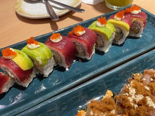 A close-up, top-down view showcases two rows of beautifully crafted sushi rolls on a textured blue plate.