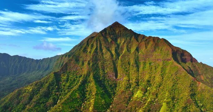 Flying to the top of the sharp peak mountain covered with lichens. White clouds in the sky at backdrop. Honolulu sceneries.