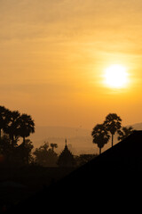 Obraz premium A peaceful sunrise with warm colors, silhouetted trees, and a temple in the background.