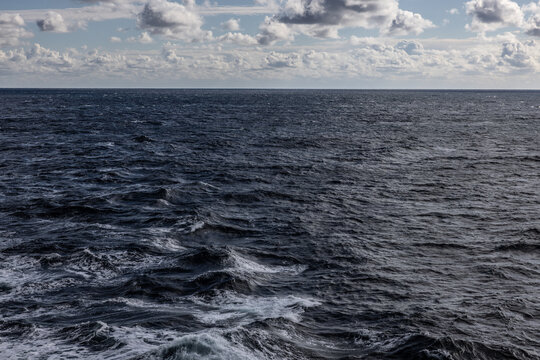 Vast Atlantic ocean horizon photograph dark gray calm ocean and white and gray cloudscape. Photo taken from moving cruise ship 