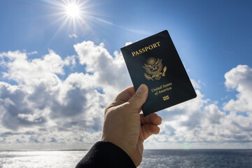 Photograph of hand holding up passport on bright beautiful day fluffy white clouds and blue sky.
