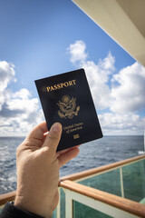 Vertical photo of hand holding up United states of America passport from the balcony of a cruise ship.