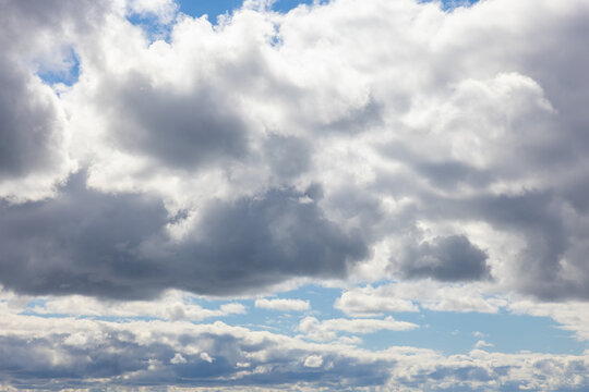 Bright cloudscape stratocumulus gray and white sunlit clouds against blue sky.