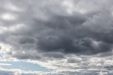 Dramatic dark and light gray fluffy cotton like clouds covering light blue sky, cloudscape textured backgrounds.