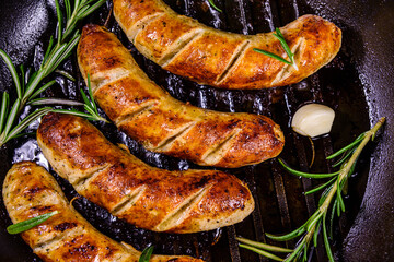Roasted sausages with rosemary twigs and garlic in a cast iron grill pan. Top view