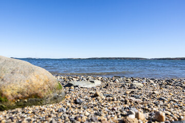 Photograph of One large boulder on a rocky pebble beach on bright sunny day and calm wavy ocean...