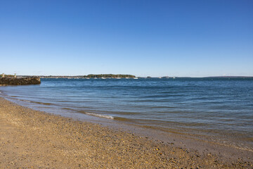Photograph of shoreline on beautiful bright sunny day with gravel sandy beach and calm flowing water.
