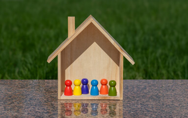 Symbolic wooden house and symbolic colorful figures of people against the background of green grass