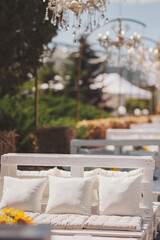 Elegant outdoor lounge setting with white cushions and dreamy chandeliers under a clear sky during a sunny afternoon.