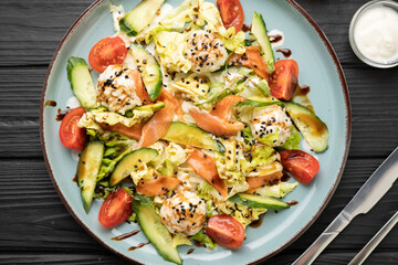 Sushi salad with rice balls, salmon slices, avocado pieces, cucumber, tomatoes, garnished with lettuce leaves on blue plate. Wooden background