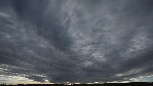 Time lapse of dramatic gray storm clouds moving above distant rolling hills
