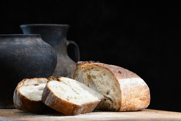 A rustic loaf of sourdough bread showcases its golden crust and soft interior on a wooden cutting board. Pottery sits in the background, enhancing the homey atmosphere
