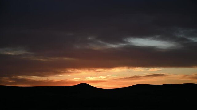 Time lapse of evening orange colored clouds after sunset above rolling hills silhouetted 
