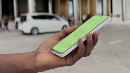 GREEN SCREEN CHROMA KEY Smartphone with a green screen held in a hand near a hotel entrance, featuring a parked car and modern urban surroundings