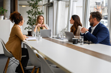 Confident businesswoman with laptop discussing report with colleagues at conference table in board room