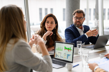 Female manager analyzing business graphs on laptop and discussing data with professional colleagues in meeting