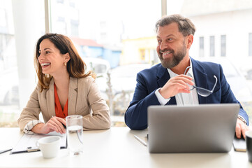 Confident male and female professional smiling and looking away while attending meeting in board room