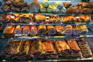 Various hams, bacons and deli meats in vacuum packaging close-up in glass display case of butcher shop.