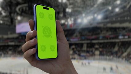 GREEN SCREEN CHROMA KEY A hand holding a phone with a green screen at a hockey game in an indoor...
