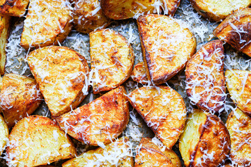 Pieces of potatoes are baked on a baking sheet, sprinkled with cheese. Background with rustic potato texture. View from above.