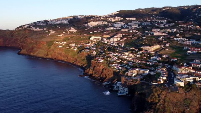 view of the beautiful coastal town Canico de Baixo on a lush hill overlooking wide sea at sunset