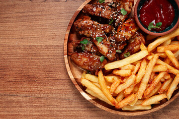 barbecue chicken wings, sprinkled with sesame seeds, with French fries, and sauce, on a wooden plate, rustic style,