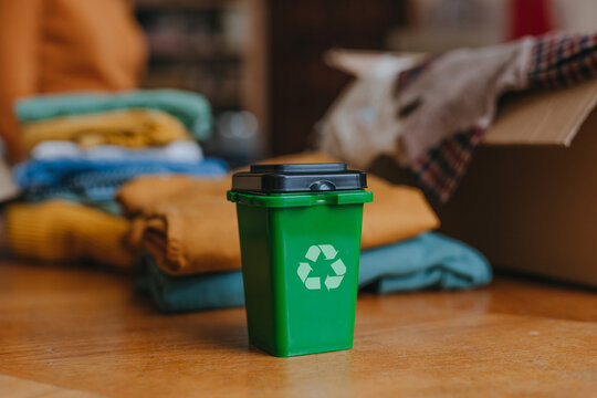 Small plastic container with symbol near old clothes sorting for upcycling