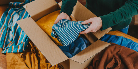 Unrecognizable man putting old clothes into box for charity or upcycling