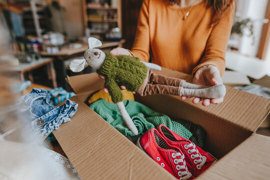 Woman sorting an old out-of-use kid toy, clothes and shoes in box for charity or upcycling