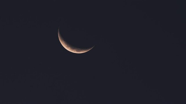 Crescent moon illuminates the darkening sky while the sun sets on the horizon