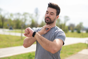Young man in sportswear checking heart rate with smartwatch outdoors
