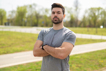 Confident young man in sportswear standing with arms crossed outdoors
