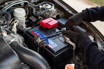 Replacing a car battery. The mechanic installs the battery, securing the battery mounting bracket...