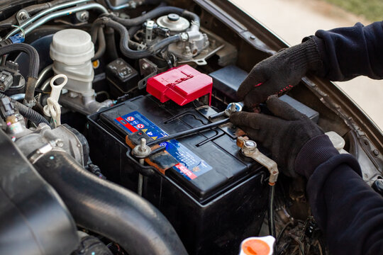 Replacing a car battery. The mechanic installs the battery, securing the battery mounting bracket with a wrench