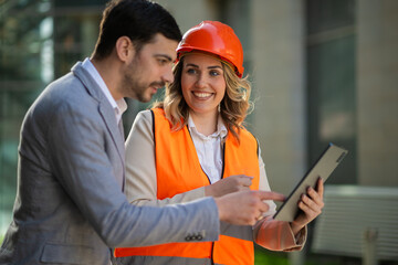 Smiling businesswoman in a safety helmet and reflective vest discussing a project with a colleague...