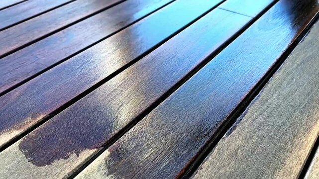 A person wiping  surplus protective finish from hard wood  surface, carefully working across the planks for an even coat under warm sunlight