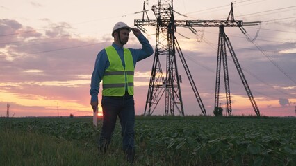 Silhouette of an electrical engineer in hard hat at sunset with tablet. business technology industry. concept electrical voltage tower towers. high voltage substation with distribution cables. energy.