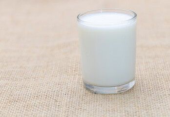 A glass of milk on a table, set against a burlap fabric background, captured through macro photography. The composition is simple, utilizing natural light to create a high-resolution
