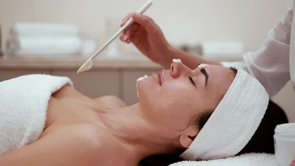 Close up beautician's hands applying anti-aging facial cream on woman client face to prevent wrinkles in spa salon. Skin care, cosmetic procedures for facial care and beauty concept. Cosmetology