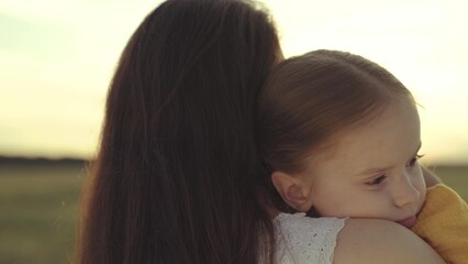 little kid hugs mother in the rays of the sun, happy family at sunset, woman loves child, take motherhood a pleasant feeling, girl daughter with mom on a journey against the sky, custody of baby.
