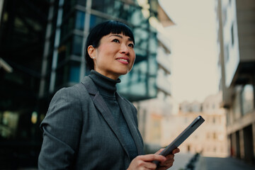 Businesswoman holding tablet and looking up at buildings in the city