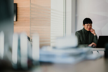 Businesswoman working on laptop in modern office with documents in foreground