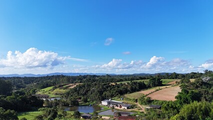 Fototapeta premium Área agrícola e florestal vista por drone, mostrando campos divididos para cultivo e faixa de mata fechada ao fundo sob céu claro