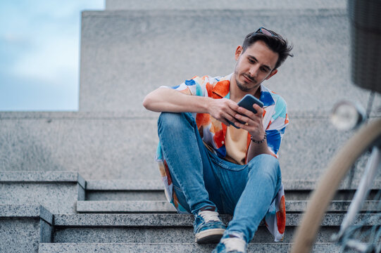 Young tourist using smartphone while sitting on city steps