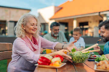 Happy senior woman sharing salad with family at garden party