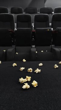Empty dark cinema with popcorn scattered on the floor, rows of black seats suggesting a messy movie experience, and a sense of solitude