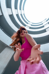 Woman in pink dancing, low angle view, in a spiral parking garage